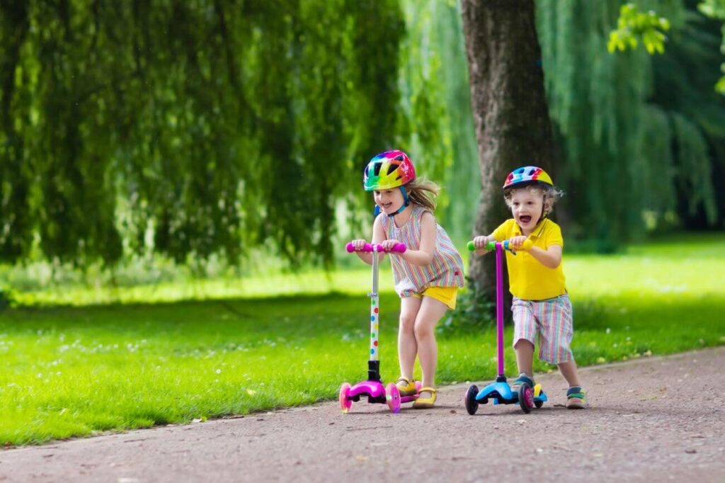 dve malé deti sa naháňajú na farebných kolobežkách