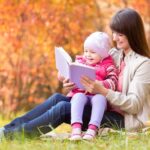 mamka číta knihu svojej dcérke v parku na tráve