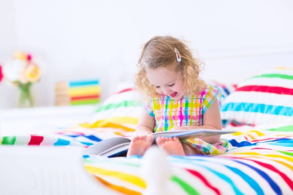 veselé dievčatko si číta knižku na farebnej posteli