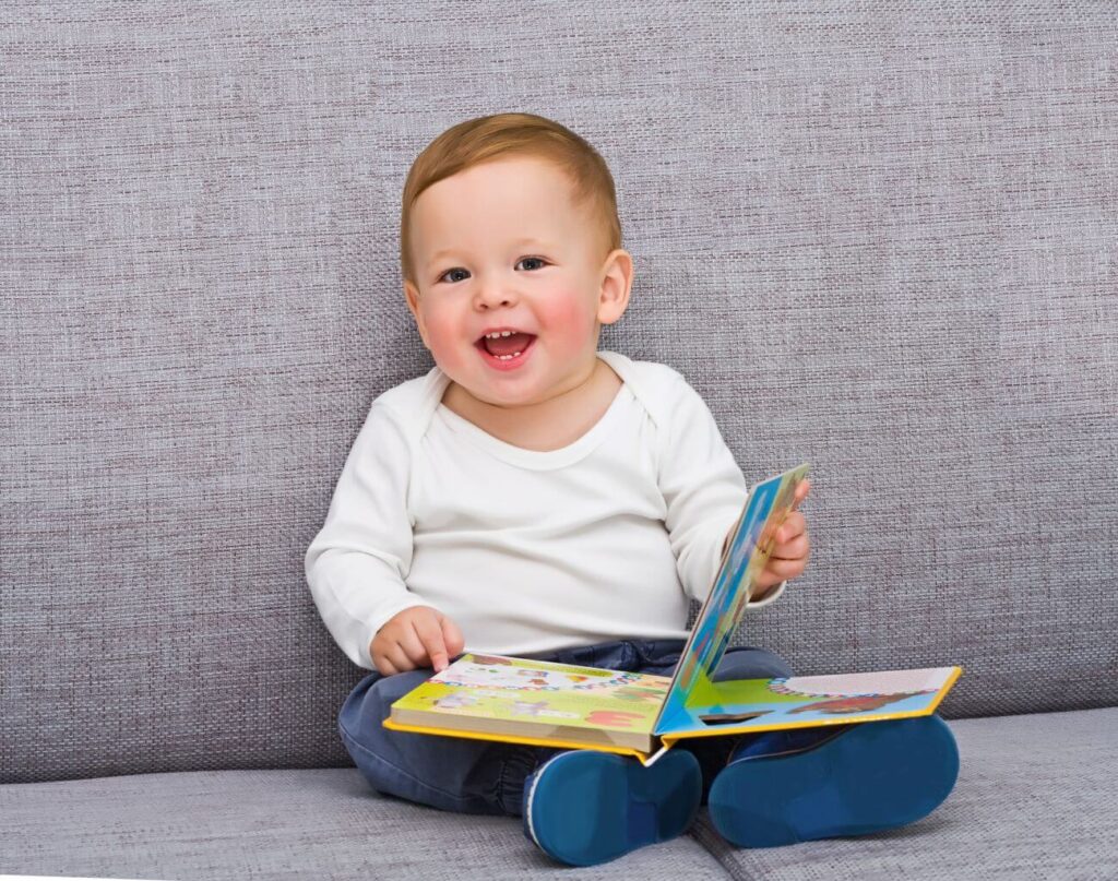 vysmiate bábätko drží knižku a pozerá sa do kamery