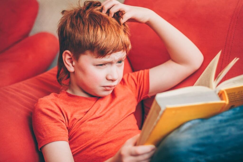 chlapec číta knihu a škrabe sa po hlave